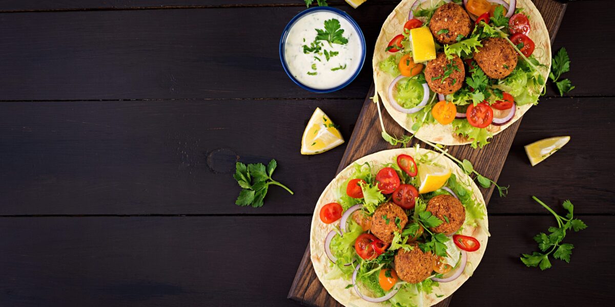 Et billede af tortillas med falaffel, salat og chili på et mørkt træbord