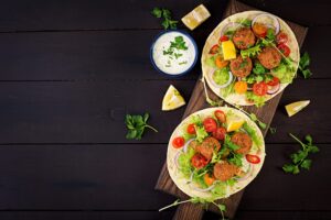 Et billede af tortillas med falaffel, salat og chili på et mørkt træbord